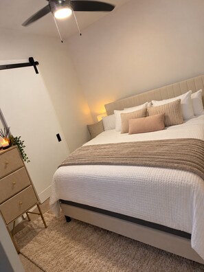 A bedroom with a bed, bedside tables, a dresser, a ceiling fan, and a wall-mounted lamp. - Cozy & Spacious 4-Bedroom Conyers Retreat with Gym (Conyers)