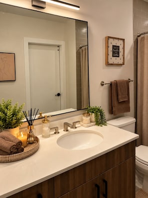 A modern bathroom with a white sink, wooden vanity, a large mirror, and a framed quote on the wall. - Cozy & Spacious 4-Bedroom Conyers Retreat with Gym (Conyers)