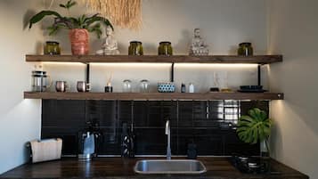 Une cuisine avec un plan de travail foncé, des étagères en bois sur lesquelles sont disposés divers pots et bouteilles, une machine à café et un évier.