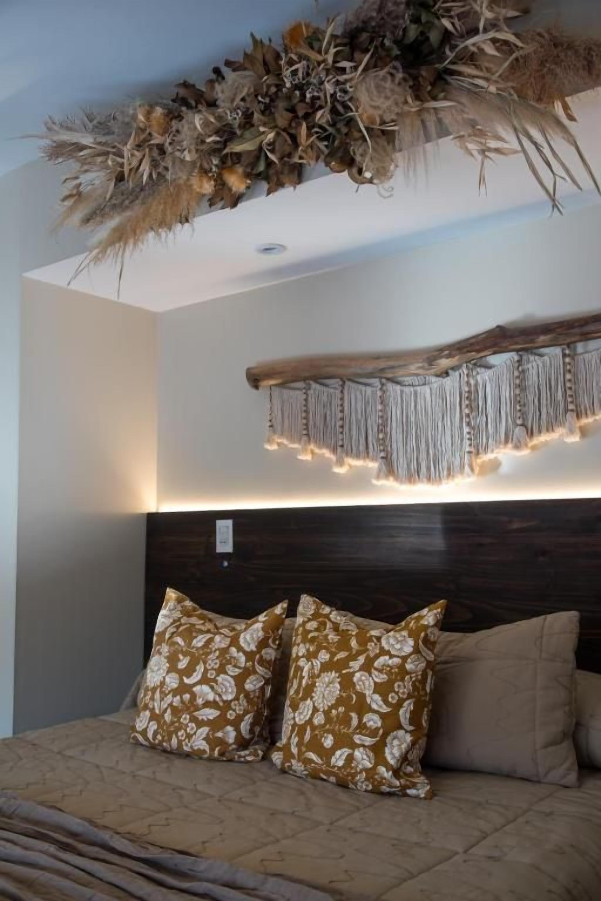 Une chambre à coucher avec un lit, deux coussins à motifs, une tête de lit sombre et une décoration murale lumineuse.