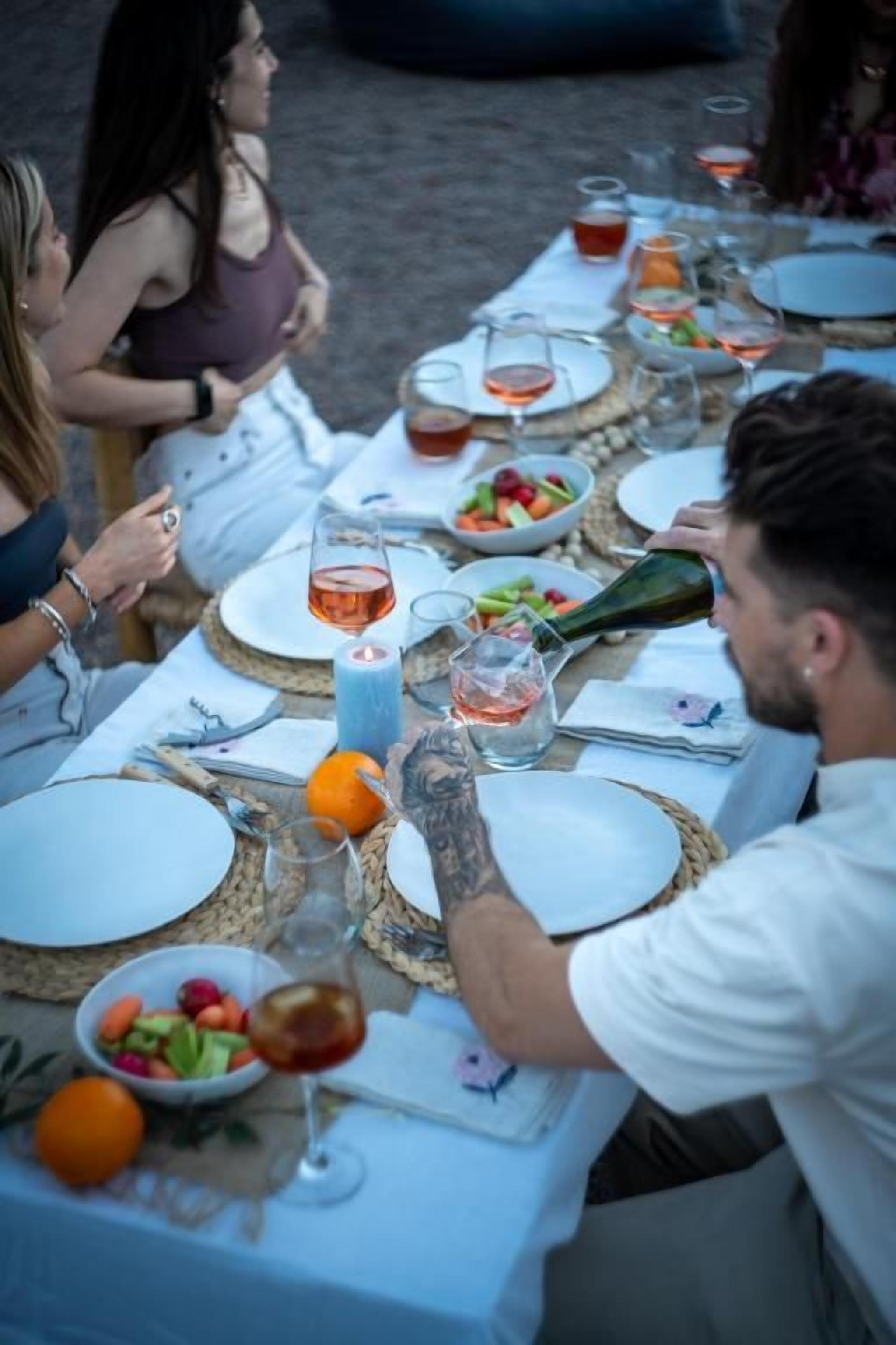 Un grupo de personas sentadas en una mesa de comedor al aire libre, con diversos platos y bebidas.