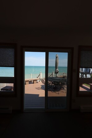 A room with a view of the ocean through a large window, a patio with a table and chairs, and a railing. - Lakefront Retreat w/ Private Beach in Madison. Sleeps 12. (Madison)