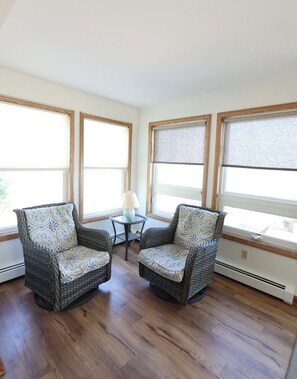 A corner room with two wicker chairs, a small table with a lamp, and large windows with blinds. - Lakefront Retreat w/ Private Beach in Madison. Sleeps 12. (Madison)