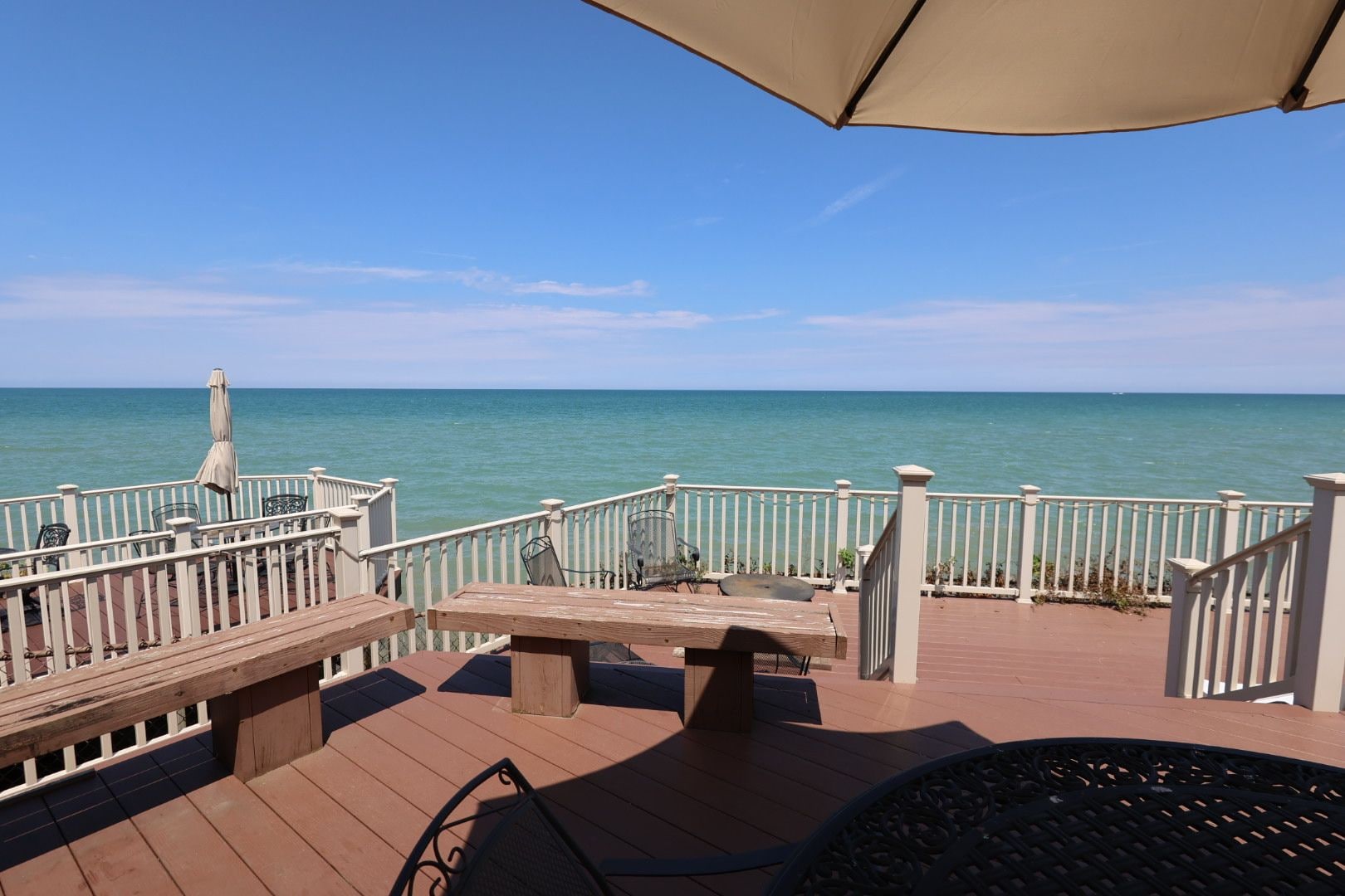 Eine Holzdar Terrasse mit Geländer, Tisch und Stühlen, mit Blick auf ein ruhiges Meer.