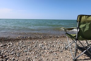 A beach with a rocky shore and calm water, a green folding chair, and a clear sky. - Lakefront Retreat w/ Private Beach in Madison. Sleeps 12. (Madison)
