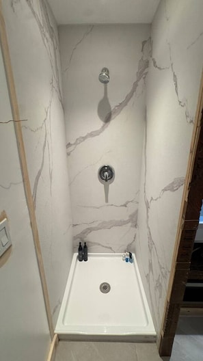 A shower stall with a marble wall, a showerhead, and a drain. - Tiny home with gazebo (San Rafael)