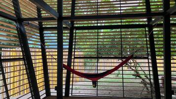 A hammock suspended between metal bars in a room with wooden flooring and a view of a bamboo fence outside.