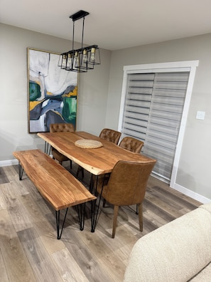 A dining area with a wooden table, leather chairs, a bench, a hanging light fixture, and a large abstract painting on the wall. - Maple House | Stylish Stay for 8 (Regina)