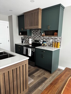 A kitchen with dark cabinetry, a brick backsplash, and a stainless steel stove. - Maple House | Stylish Stay for 8 (Regina)