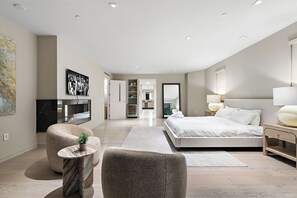 Una habitación de hotel moderna con una cama grande, una zona de estar con una mesa redonda y un televisor.