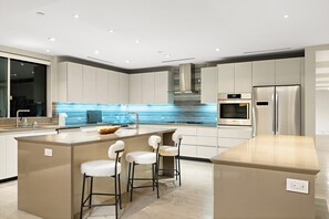 Eine moderne Küche mit einer zentralen Kochinsel, Barhocker, einem Backofen und einem Edelstahl-Kühlschrank.
