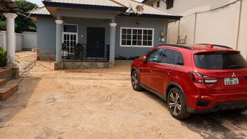 A residential property with a paved driveway, a house with a tiled roof, and a red SUV parked in the driveway.