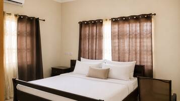 A standard hotel room with a single bed, two bedside tables, a chair, and a window with curtains.
