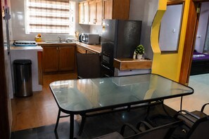 Una cocina compacta con armarios de madera, un cubo de basura de acero inoxidable, una mesa de vidrio y un refrigerador.