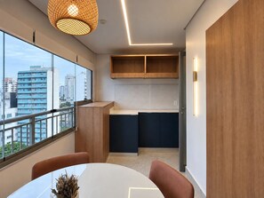 A modern kitchen with built-in cabinets, a dining area with a table and chairs, and a large window offering a city view. - Cuidado em Cada Detalhe | Ao lado do Nubank Parque (São Paulo)