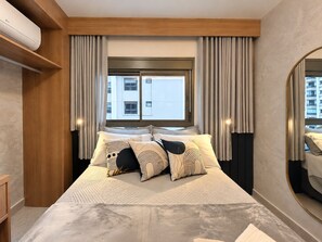 A hotel room with a large bed, a window with curtains, a built-in air conditioning unit, and a mirror on the wall. - Cuidado em Cada Detalhe | Ao lado do Nubank Parque (São Paulo)