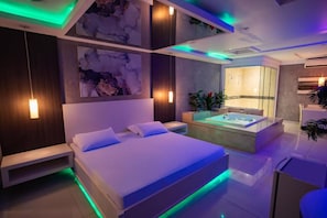 Un dormitorio moderno con una cama grande, una bañera integrada e iluminación ambiental.