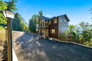 A two-story house with a stone foundation, a wooden exterior, and a driveway leading to a gated entrance. - Brand new lux cabin + indoor pool +mountain views (Gatlinburg)