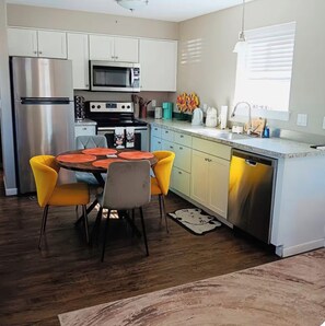 A modern kitchen with stainless steel appliances, a dining table with yellow chairs, and a window with blinds. - Mr. Fatness Home: A puurrrfet place to relax & make unique memories 🐾🐈🥰 (Kittitas)