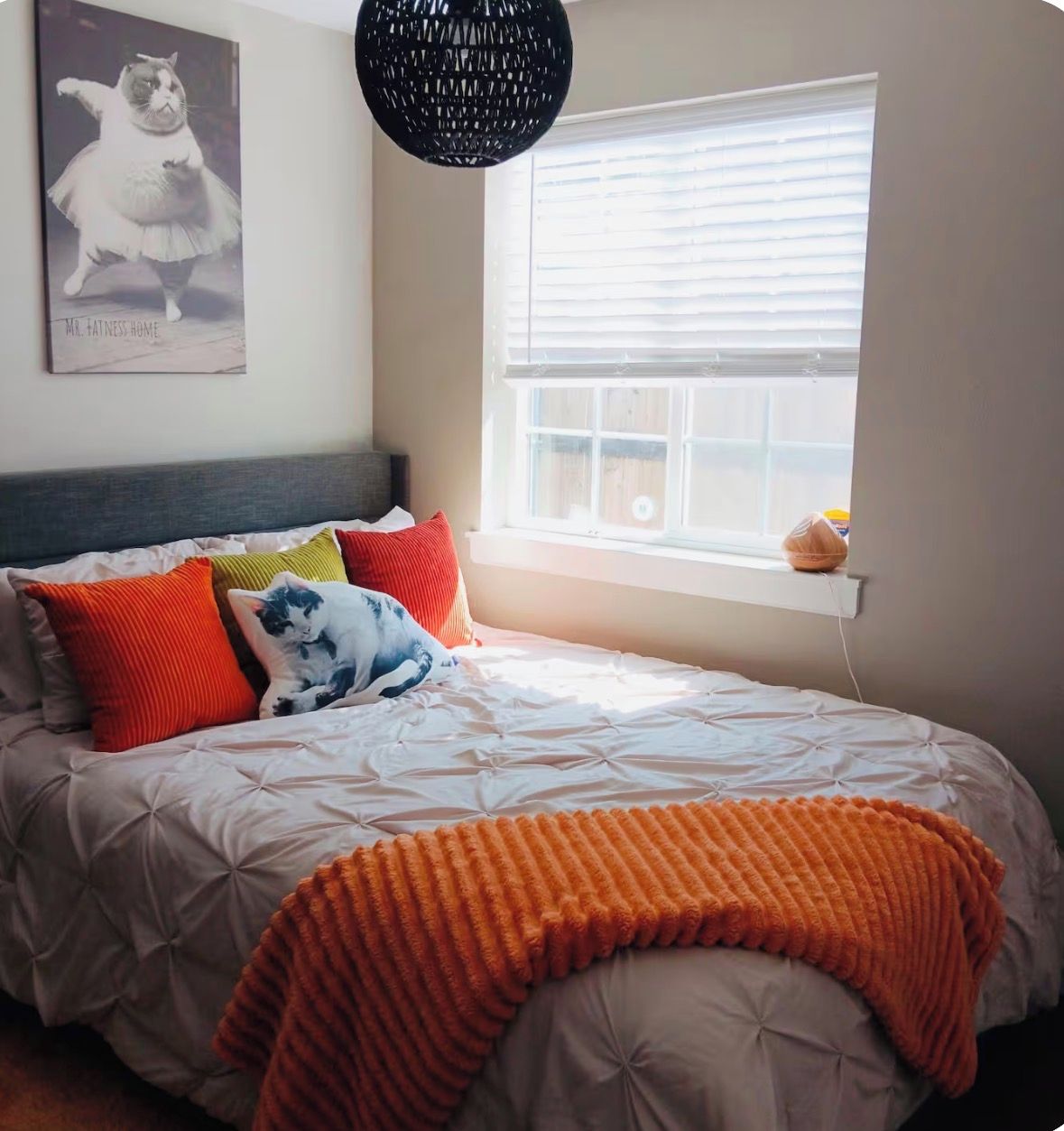 A bedroom with a bed, pillows, a blanket, a wall-mounted picture, and a window with blinds.