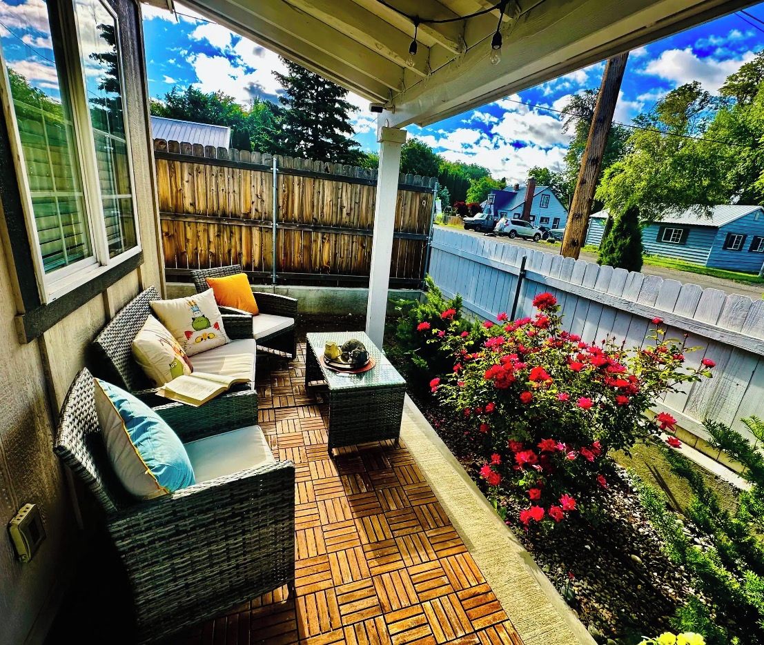 A covered patio with wicker furniture, a small table, and a flower bed with red flowers.