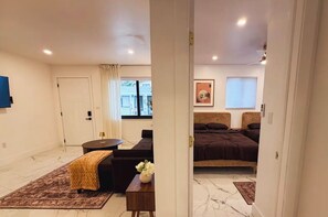 A hotel room with a bed, a sofa, a small table with a vase, a window with curtains, and a door. - Luxury Miami Stay • Near Wynwood/Design District (Miami)