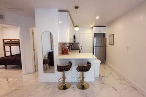 A modern kitchen with a central island, two bar stools, a refrigerator, and a microwave. - Luxury Miami Stay • Near Wynwood/Design District (Miami)