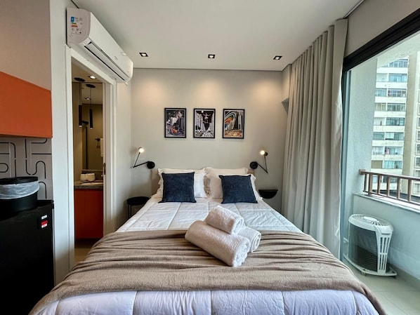 A hotel room with a bed, artwork on the wall, and a view of the city. - My One 901 (São Paulo)