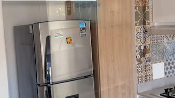 Ein Edelstahl-Kühlschrank mit Wasserspender, neben einem Holzschrank und einer gefliesten Spritzschutzwand.