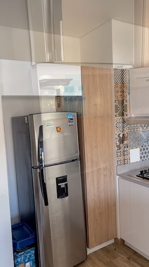 Een roestvrijstalen koelkast met een waterdispenser, naast een houten kast en een betegelde achterwand.
