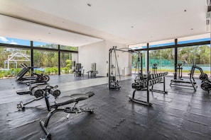 A modern gym with various exercise equipment, large windows, and a view of an outdoor tennis court. - Xpuha Villa, Private Pool and Jungle, Near Beach (Xpu Ha)