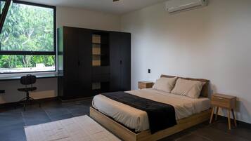 A bedroom with a bed, a desk, a wardrobe, and a window with a view of greenery.
