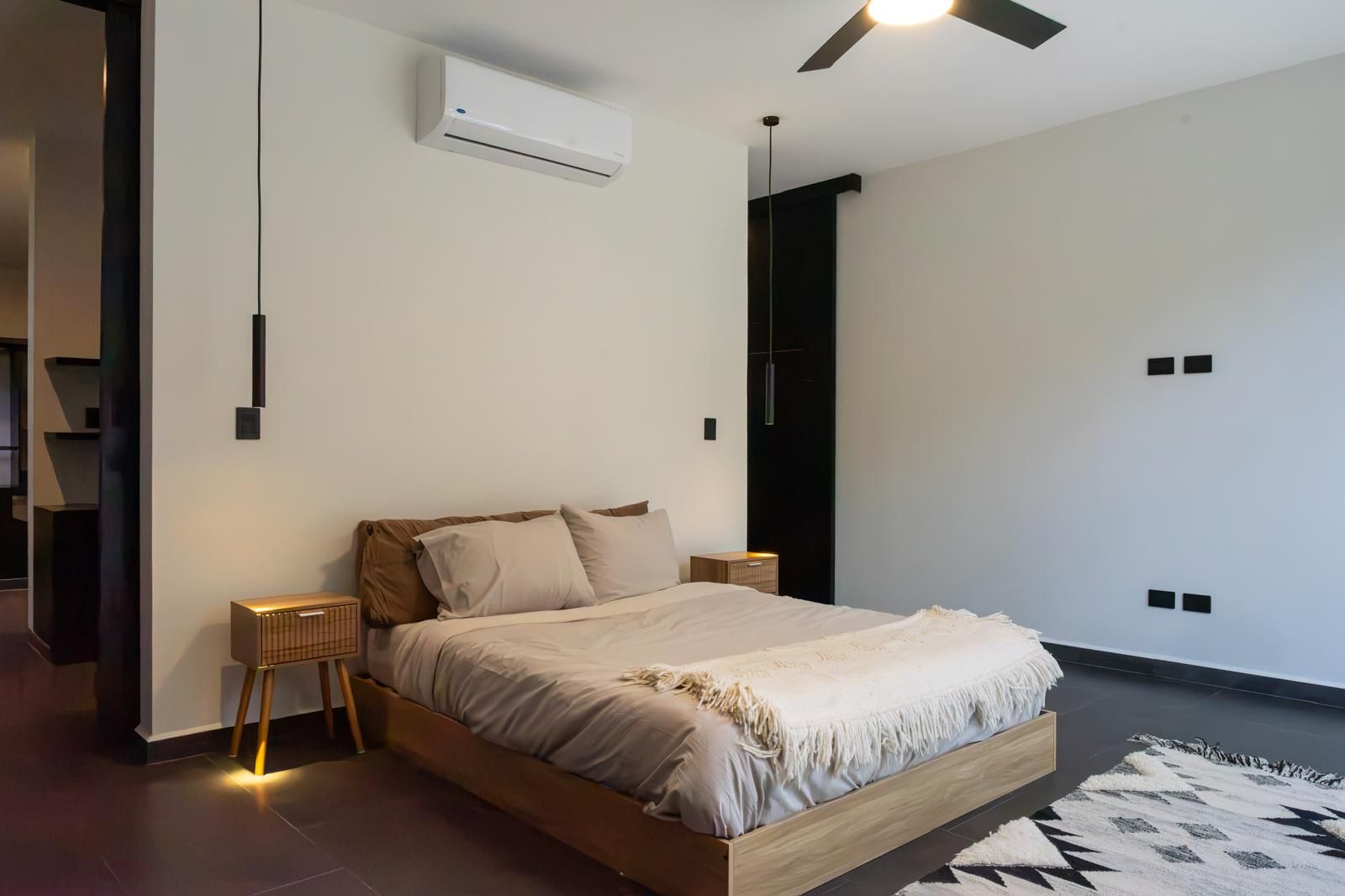 A modern bedroom with a bed, bedside tables, an air conditioning unit, and a ceiling fan.