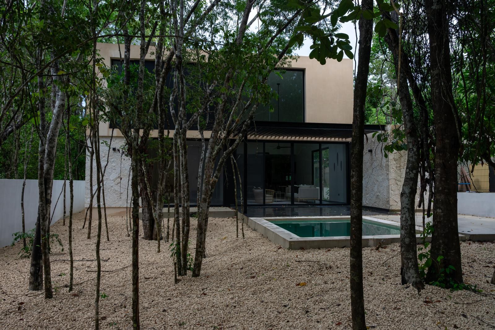 A modern house with a swimming pool, surrounded by trees and gravel.
