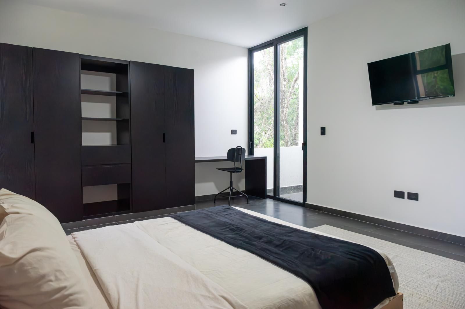Une chambre à coucher moderne, équipée d’un lit, d’une armoire, d’un bureau et d’un téléviseur.