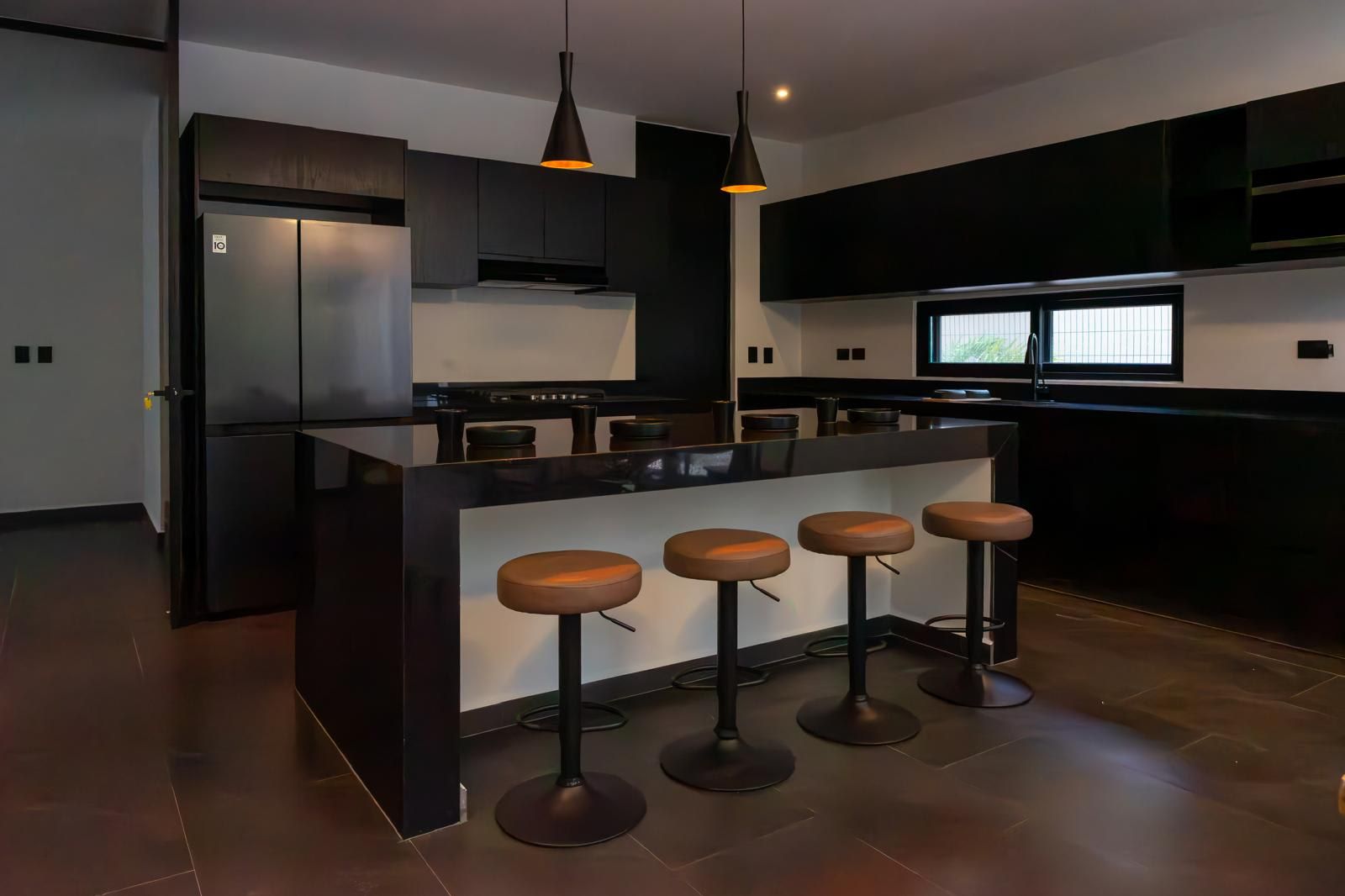 Une cuisine moderne dotée d’un îlot central, de tabourets de bar et de luminaires suspendus.