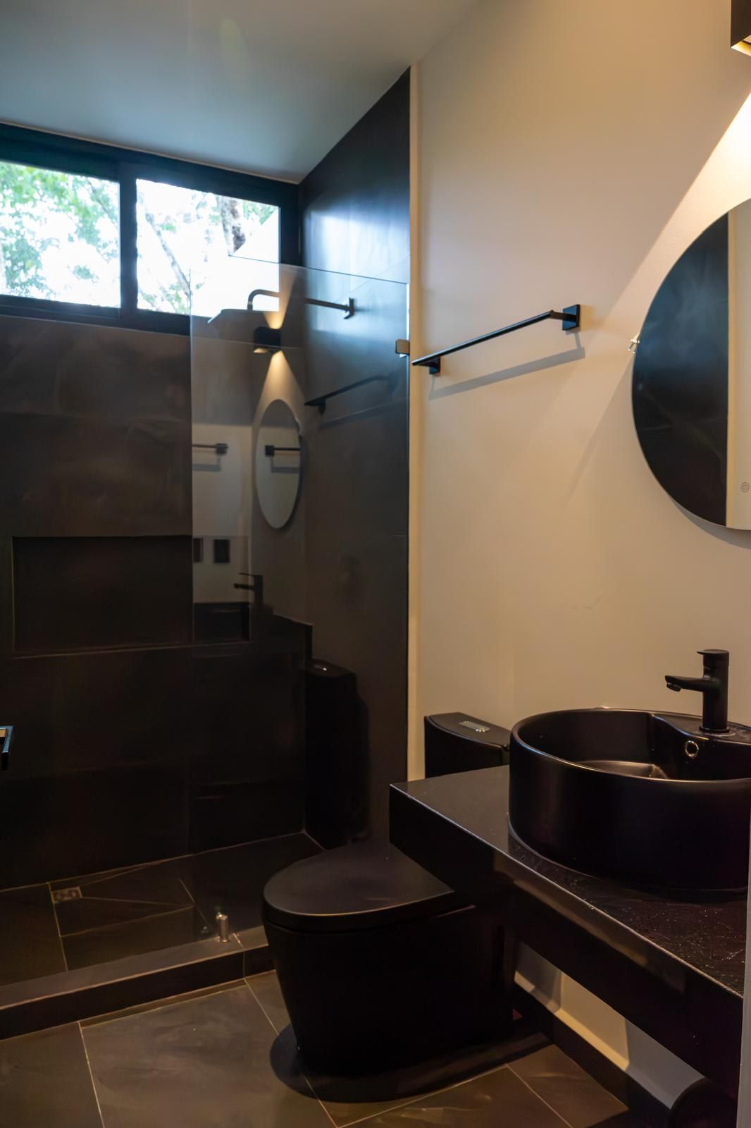 A modern bathroom with a large mirror, a round sink, and a toilet.