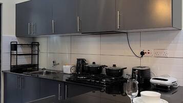 Une cuisine moderne avec des meubles de couleur sombre, un plan de travail noir et un îlot central agrémenté d’assiettes blanches et d’un verre à vin.
