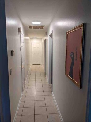 A narrow hallway with a tiled floor, a door at the end, and a framed picture on the wall. - Child-Friendly Retreat Near Charleston, 2 (Hanahan)