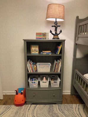 A room with a bookshelf, a lamp, a bed, and a storage bin. - Child-Friendly Retreat Near Charleston, 2 (Hanahan)