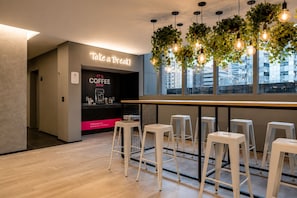 A modern coffee bar with a sign that reads 'Take a Break! It's Coffee Time,' and a seating area with white stools. - On Paulista 1921 (Vila Mariana)