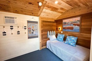 A cabin with a wooden ceiling, a bed with patterned pillows, a wall-mounted heater, and a framed picture of a lake. - Lakefront, dog-friendly house with amazing view, dock, 2 kayaks & canoe (Isle La Motte)