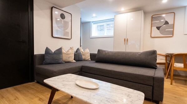 A modern living room with a grey sectional sofa, a marble coffee table, and a wooden dining table.