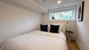 A bedroom with a bed, a window, and a bedside table with a lamp.
