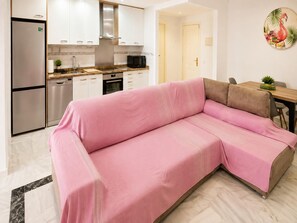 A modern living room with a pink sofa, a wooden dining table, and a kitchen in the background. - Apartment with private patio in Marbella (Marbella)