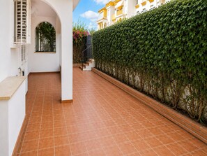 A corridor with a tiled floor, a white wall with a window, and a green hedge. - Apartment with private patio in Marbella (Marbella)