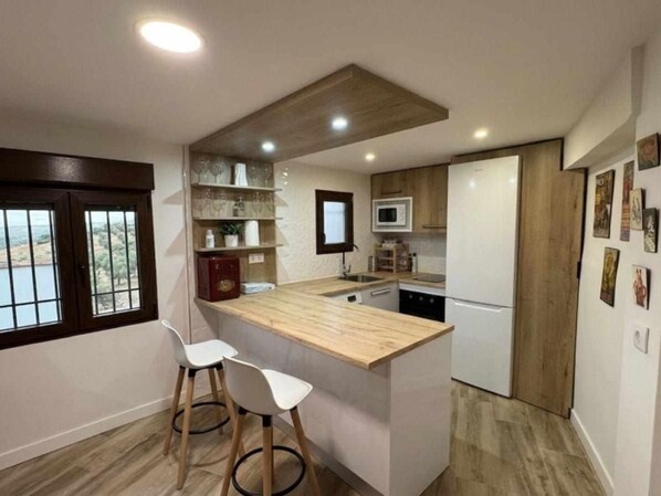 A compact kitchen with a wooden island, two white bar stools, a microwave, a refrigerator, and a window with a view.