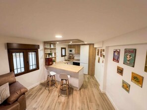 A compact living space with a kitchenette, a dining area with stools, and a sofa.