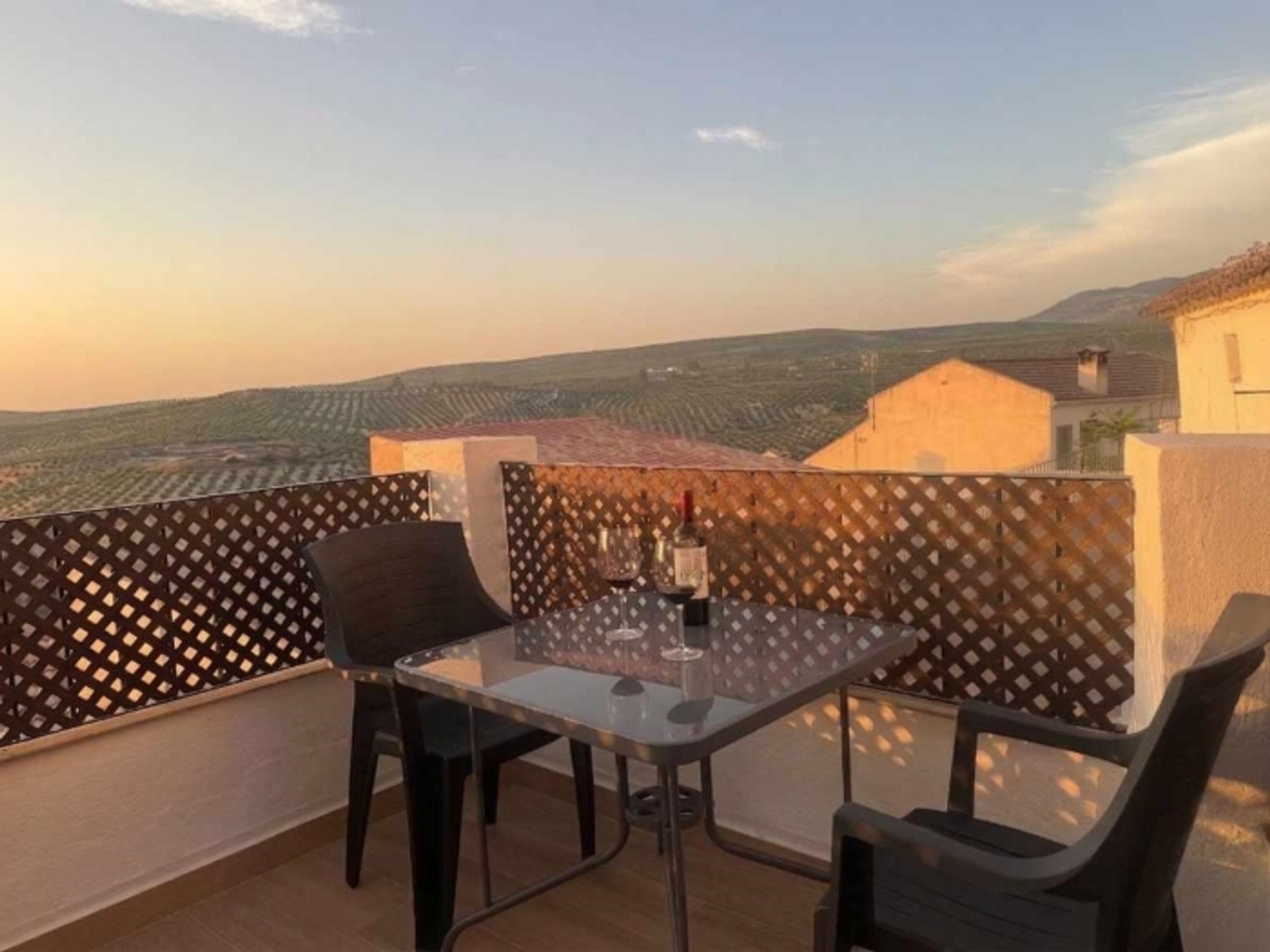Een balkon met een tafel en stoelen, met uitzicht op een wijngaard.