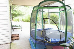 A trampoline with a safety net enclosure, a picnic table, and a covered porch area. - Child-Friendly Retreat Near Charleston (Hanahan)